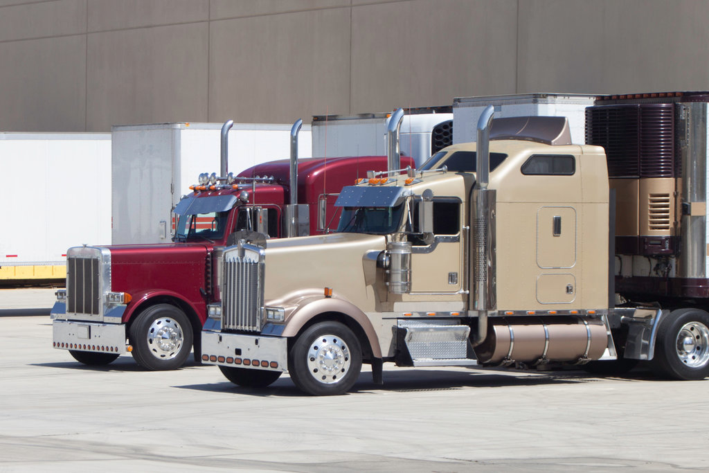 Two big rig trucks waiting at the warehouse dock to be unloaded and loaded with cargo.